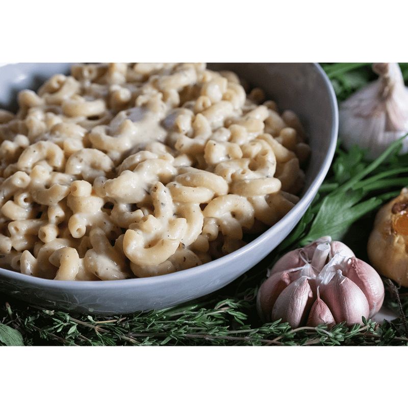Bowl of creamy vegan mac and cheese on a bed of herbs and garlic