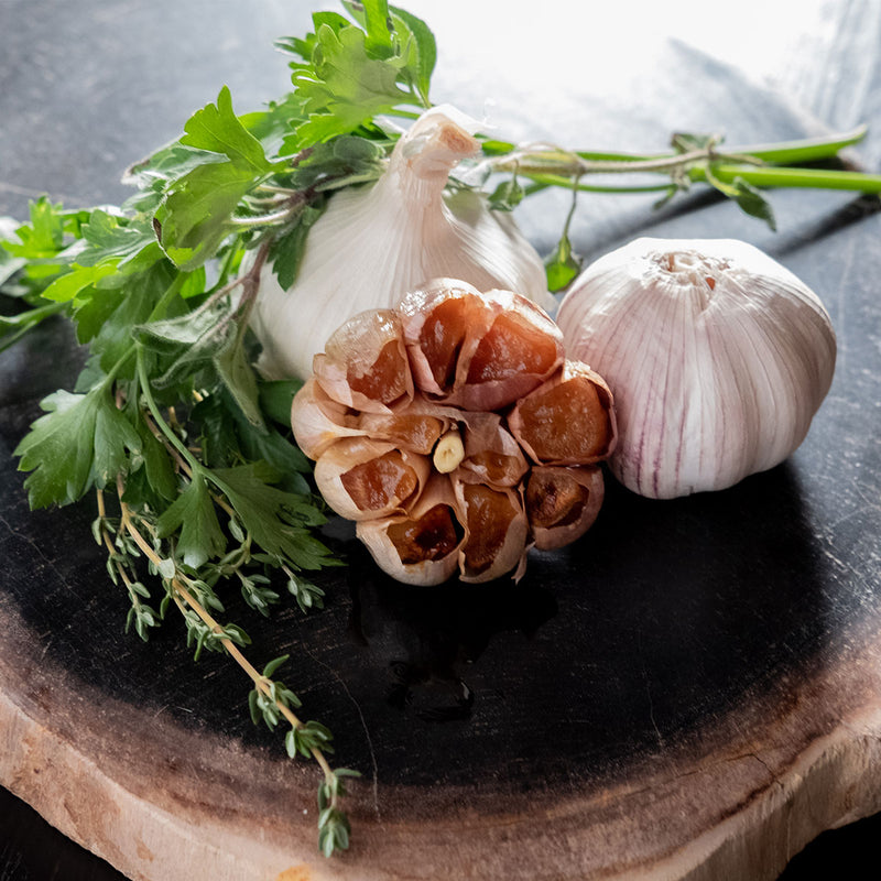 Roasted Garlic cut open next to Italian herbs